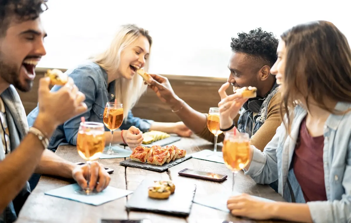 Grupo de estudiantes compartiendo tapas y bebidas en una mesa de bar con ambiente animado