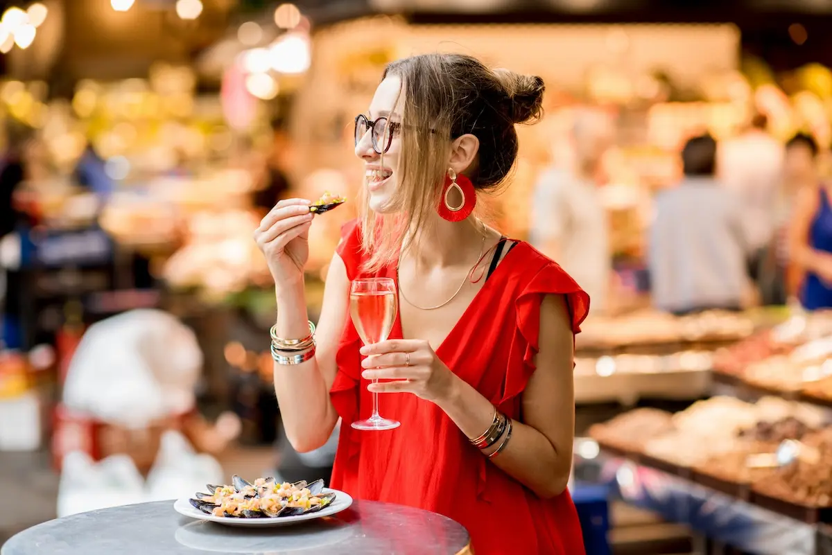 Joven disfrutando de una tapa y una bebida en un mercado gastronómico con ambiente cálido