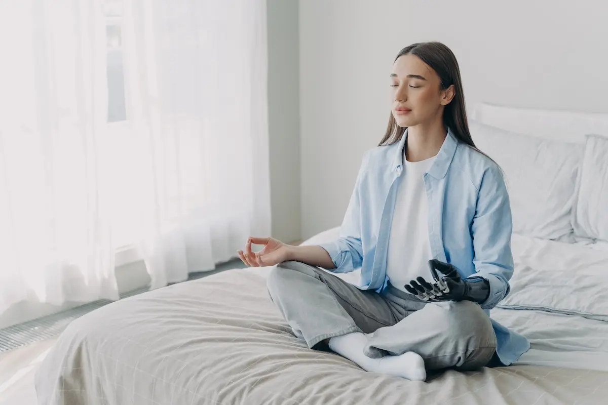 Joven sentada sobre la cama practicando meditación y respiración en una habitación luminosa