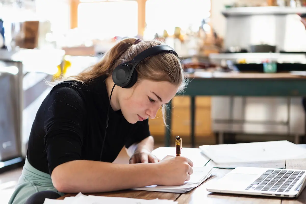 Estudiante con auriculares concentrada mientras estudia con un portátil y una libreta